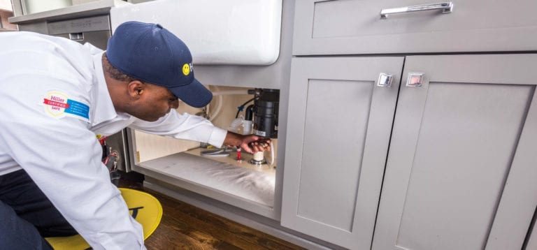 technician working on jammed garbage disposal under kitchen sink