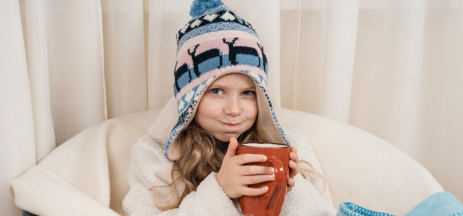 Child Sitting Inside With Hot Drink and Winter Clothes