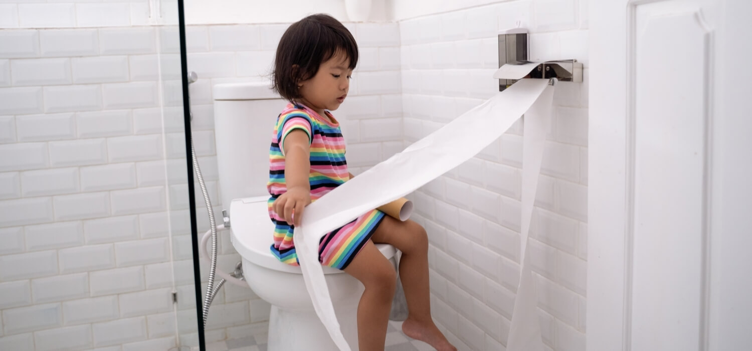 Little Girl Sitting on Toilet Pulling Out All of the Toilet Paper