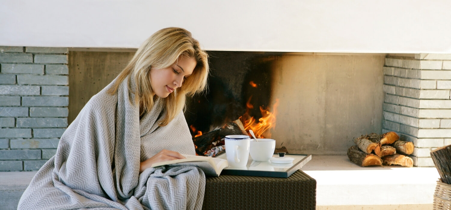 Lady Cold Reading a Book Inside With a Blanket by the Fire