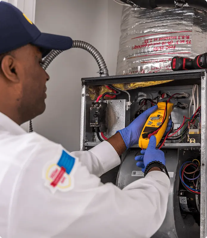 A Hiller technician using a digital multimeter to test a Trane inverter control board.